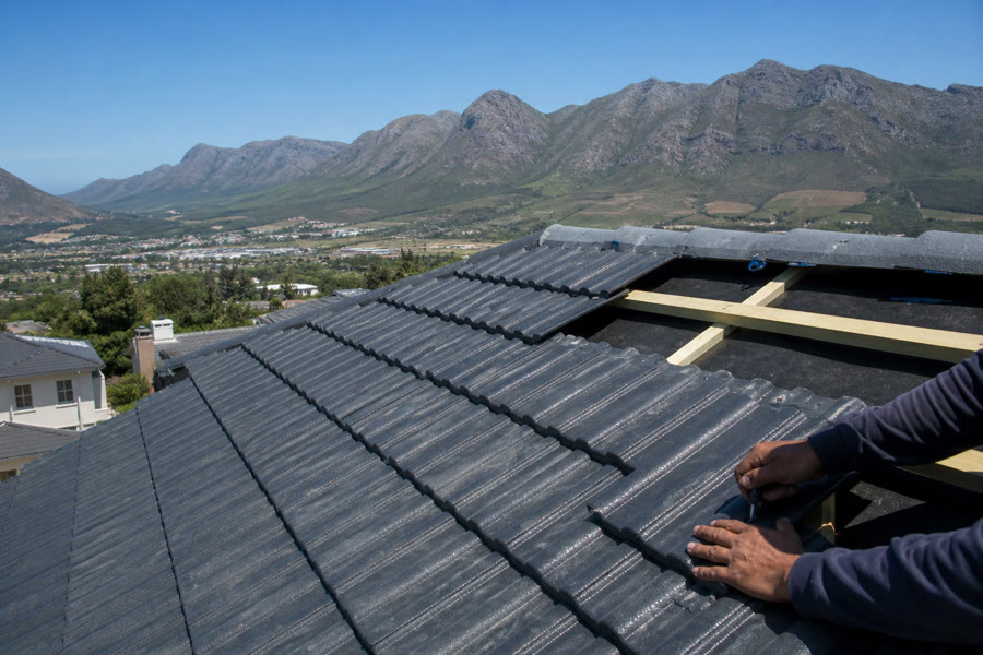 Roof tiles being fitted on battens over underlay, Helderberg behind the pitch.